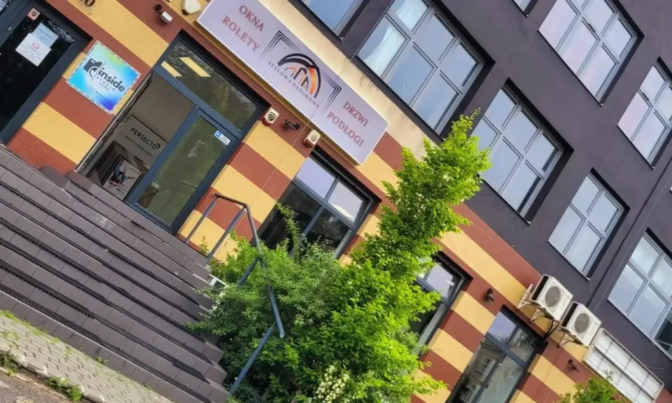 Elegancki budynek z oknami i drzwiami, z zielenią przed wejściem.