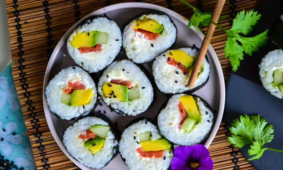 Assiette de makis frais, parfaits pour une recette sushi maison. Avocat, saumon et concombre roulés dans du riz et des algues, parsemés de graines de sésame.