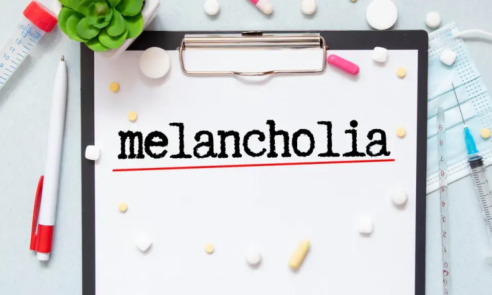 Na kartce widnieje napis "melancholia". Wokół leżą tabletki, strzykawka i maseczka, sugerując walkę z tym stanem.