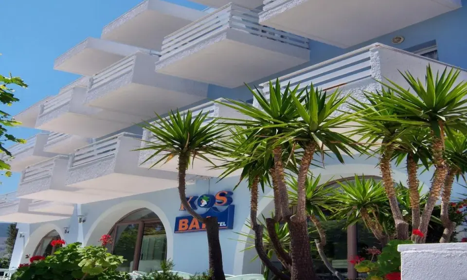 Hotel na Krecie z białymi balkonami i palmami.