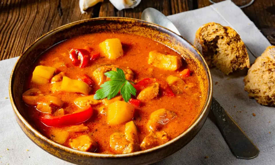 Aksamitna zupa gulaszowa, przepis babci, z kawałkami mięsa, ziemniaków i papryki, udekorowana natką pietruszki.