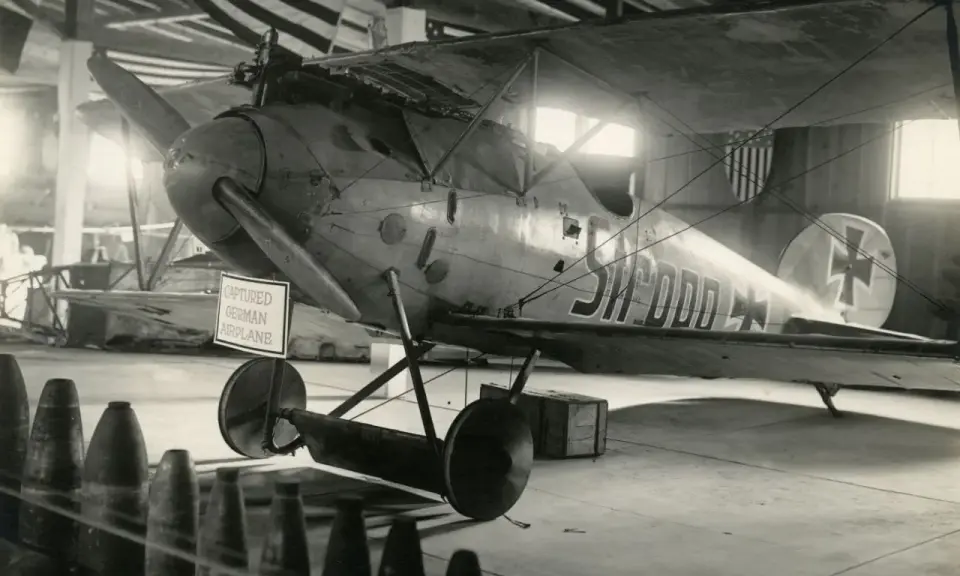 Gefangenes Albatros Flugzeug mit deutscher Kennung in einer Halle, hinter ihm US-Flaggen.