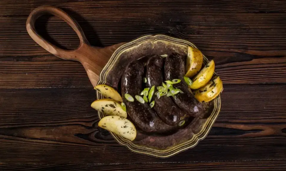 Kaszanka z piekarnika podana z pieczonymi ziemniakami i szczypiorkiem na ozdobnym talerzu.