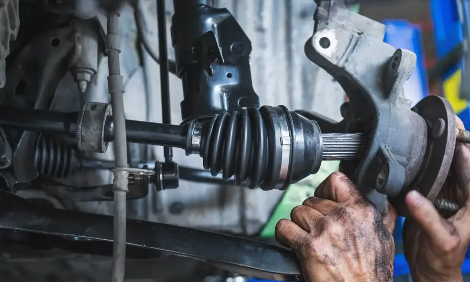Mechanik wymienia uszkodzoną półoś, która powoduje wibracje. Widać gumową osłonę przegubu i zębaty wałek.