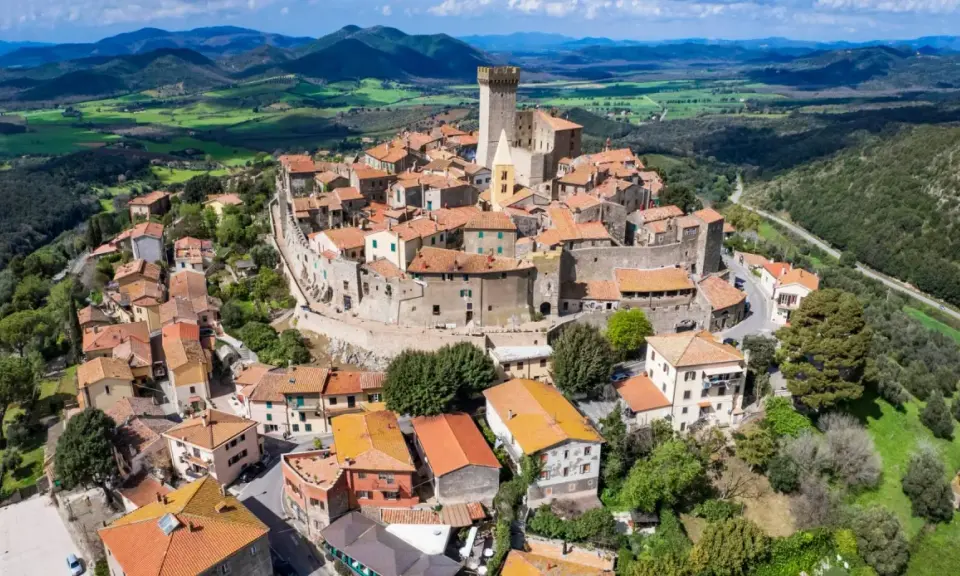 Un borgo medievale con un castello domina le colline toscane. Perfetto per un weekend in Toscana, tra tetti rossi e panorami mozzafiato.