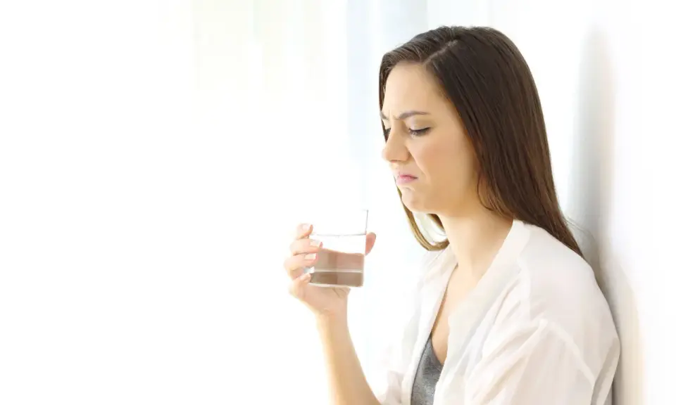 Kvinna med grimaserande ansikte håller ett glas vatten, möjligen ett symptom på oral galvanism.