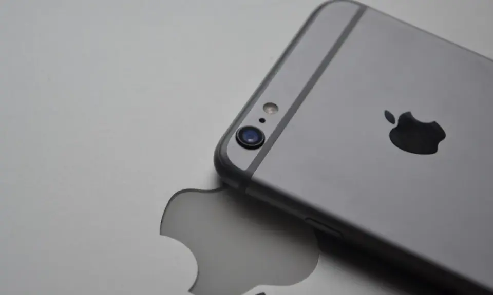 Srebrny iPhone leży na tle z wyciętym logo Apple, symbolizując spójność ekosystemu Apple.