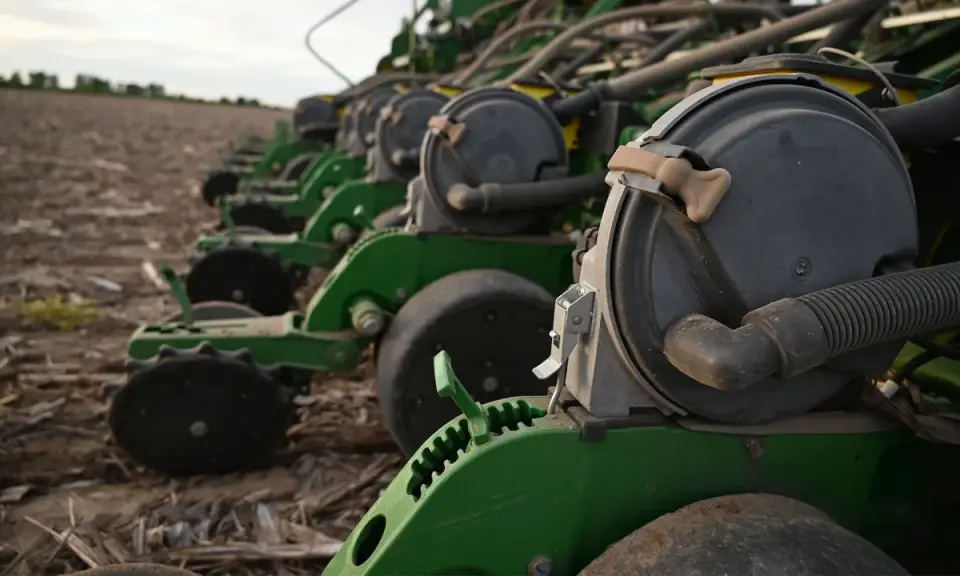 A row of green planters sits in a field, ready for planting. These machines are essential for farmers, contributing to the average hours on a tractor per year.