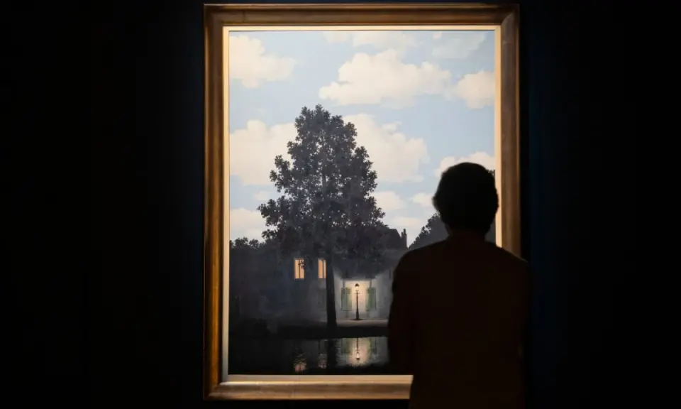 A person gazes at Magritte's "Empire of Light," a surreal scene of a house illuminated by a streetlamp under a daytime sky.