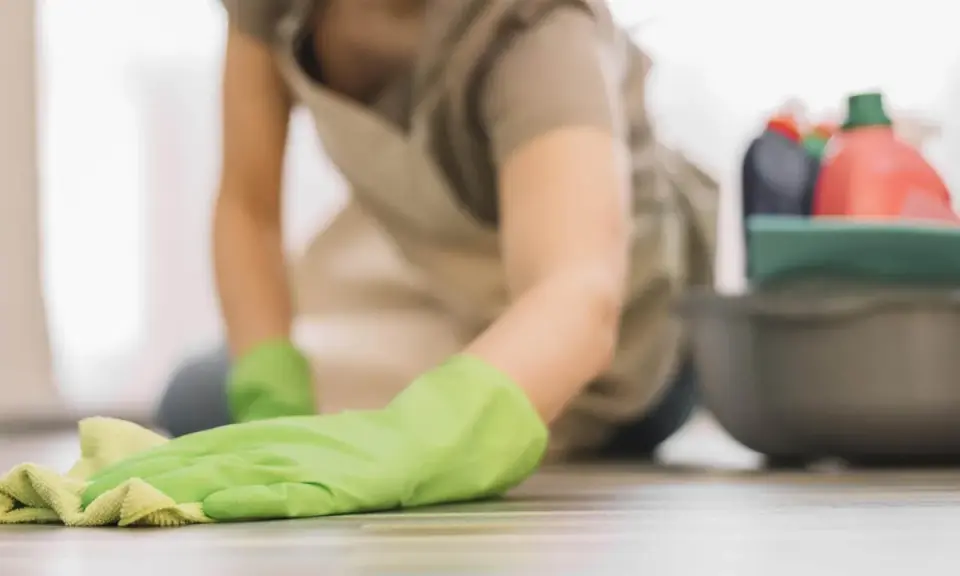 Rękawiczka w zielonym kolorze czyści linoleum. Obok miska z płynami do sprzątania, w tym ocet.