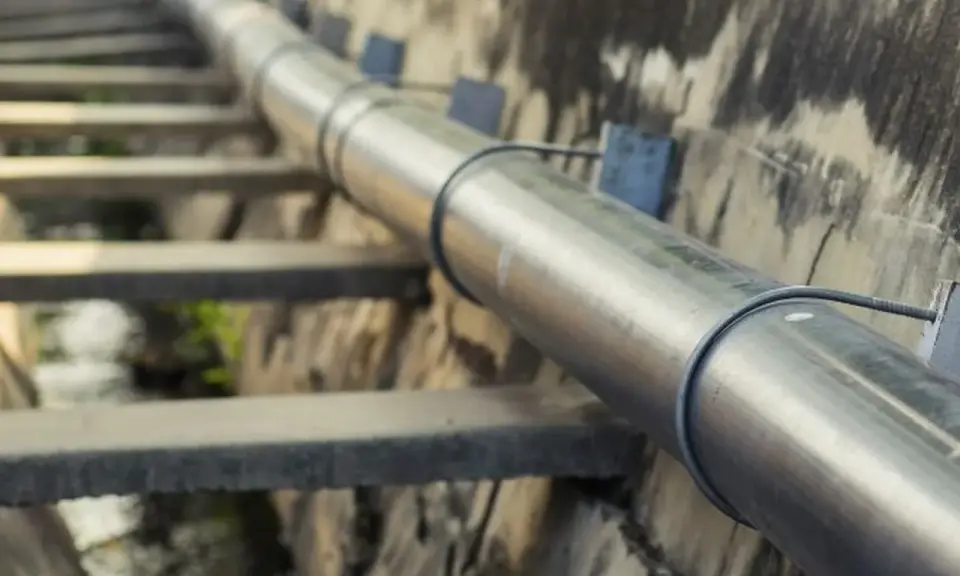 Długi, metalowy rurociąg biegnie wzdłuż betonowego koryta. To ważna kanalizacja tłoczna, transportująca płyny.