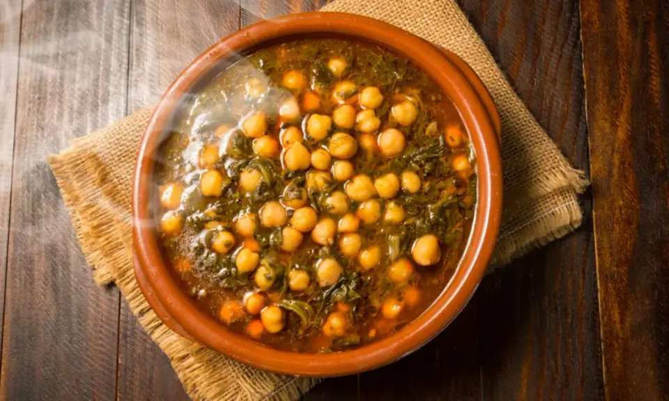 Cazuela de barro con garbanzos y espinacas, humeante y lista para servir. Se puede poner cazuela de barro en la vitro para cocinar este delicioso plato.