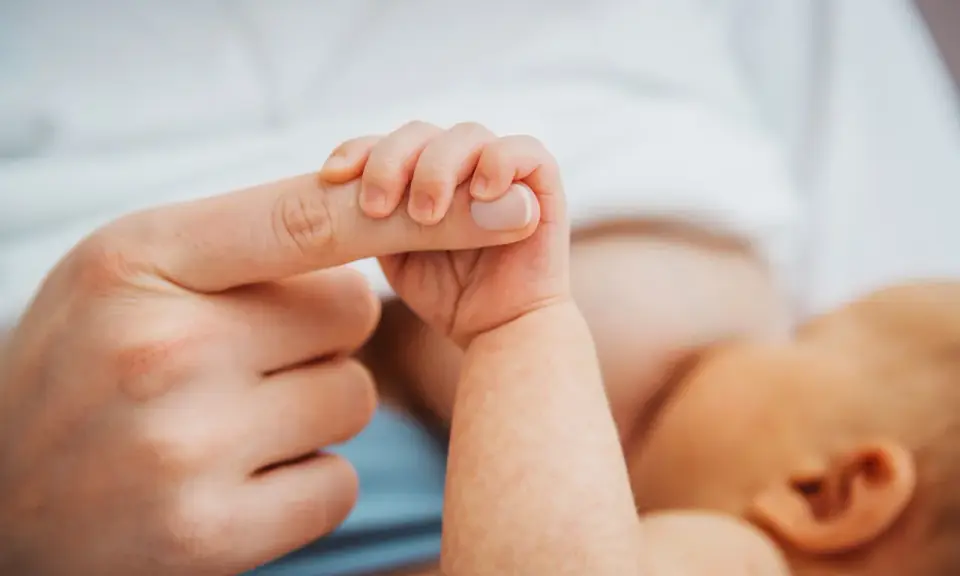 Dłoń noworodka ściska palec dorosłego. Delikatny uścisk, który budzi pytanie: czy można przekarmić noworodka?
