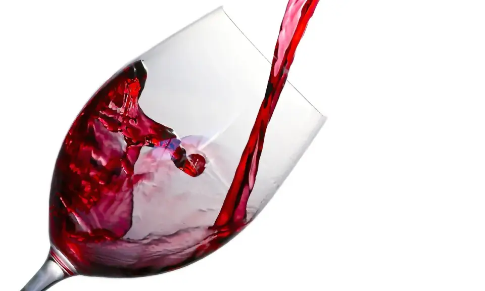 Un jet de vin rouge tourbillonne dans un verre à beaujolais, créant des éclaboussures vibrantes.