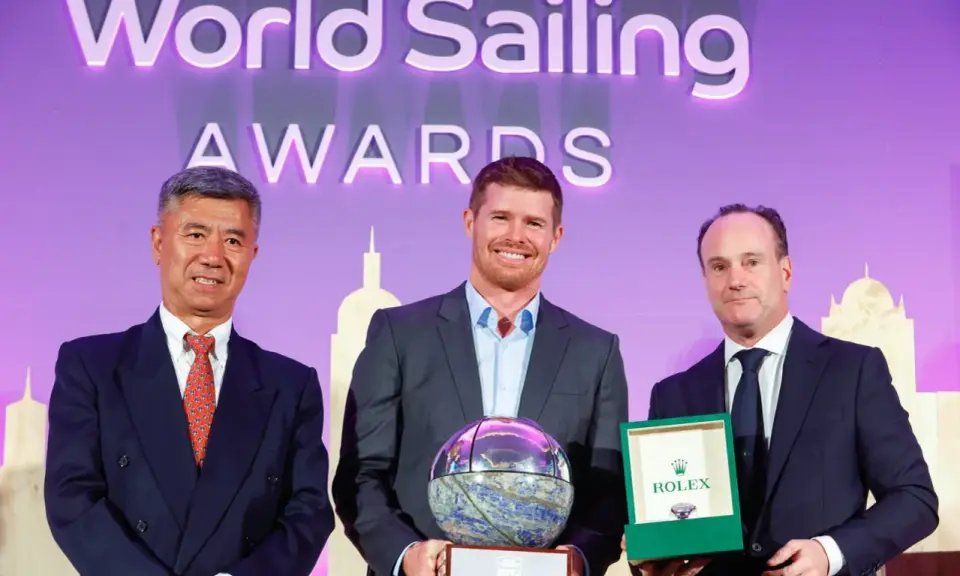 Tom Slingsby mit Auszeichnung bei den World Sailing Awards. Er hält eine Trophäe, daneben zwei Männer mit Geschenken.