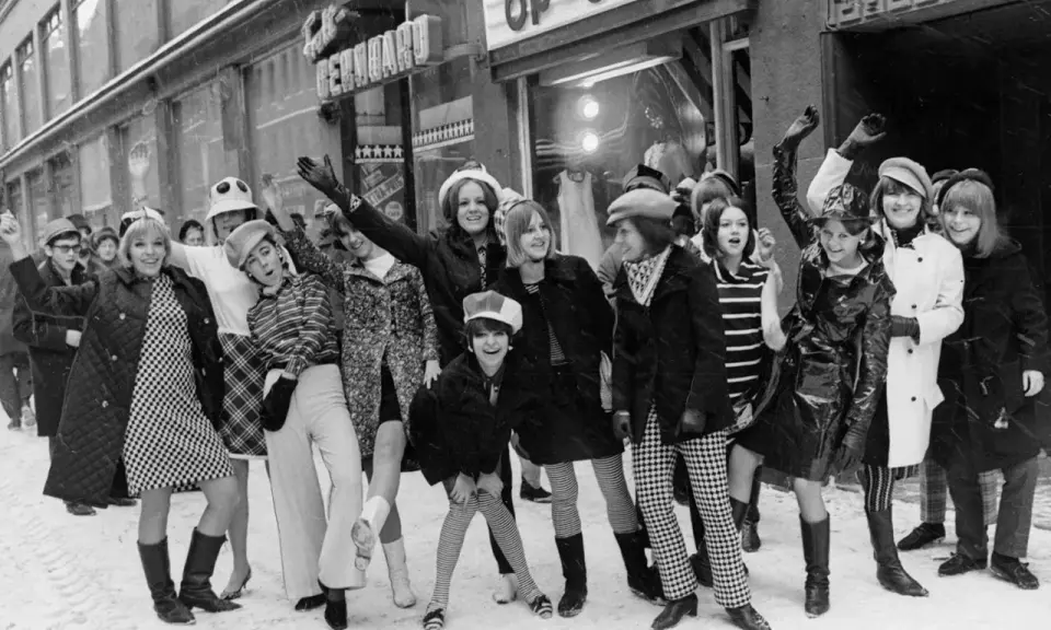 Ungdomar i trendiga kläder utanför en op-shop i Sverige 1960. Snö på marken och glada miner.
