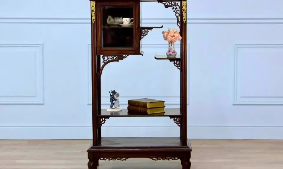 Étagère en bois sombre ornée de motifs dorés, rappelant le style de Gabriel Viardot. Elle présente des tasses dans une vitrine, des livres et des fleurs.