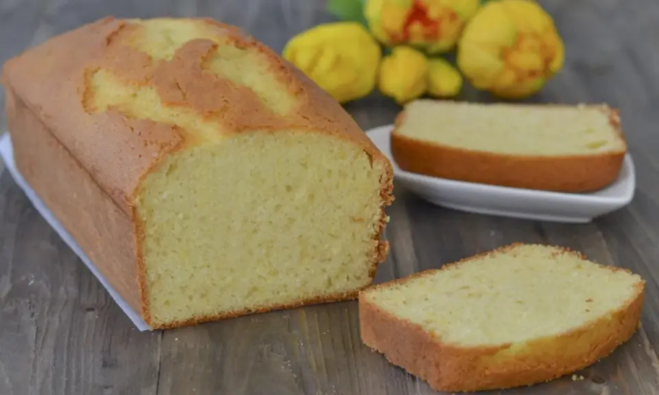 Un soffice plumcake al limone, dorato e profumato, pronto per essere gustato. Due fette sono già state tagliate, invitando a un assaggio.
