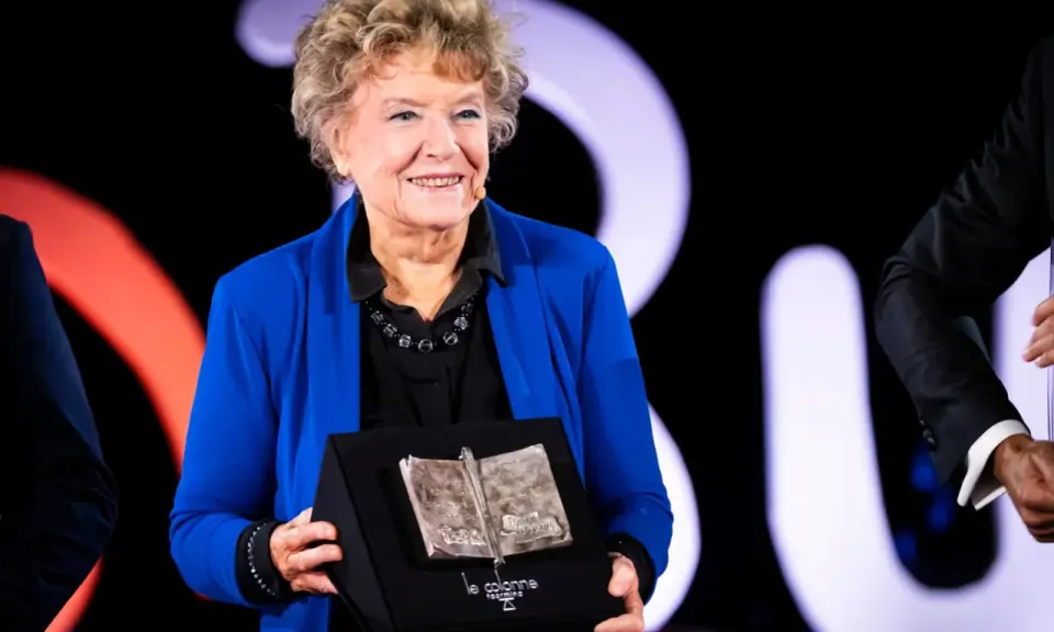Una donna sorride sul palco, tenendo un premio a forma di libro aperto. Un simbolo di ispirazione per le libere donne.