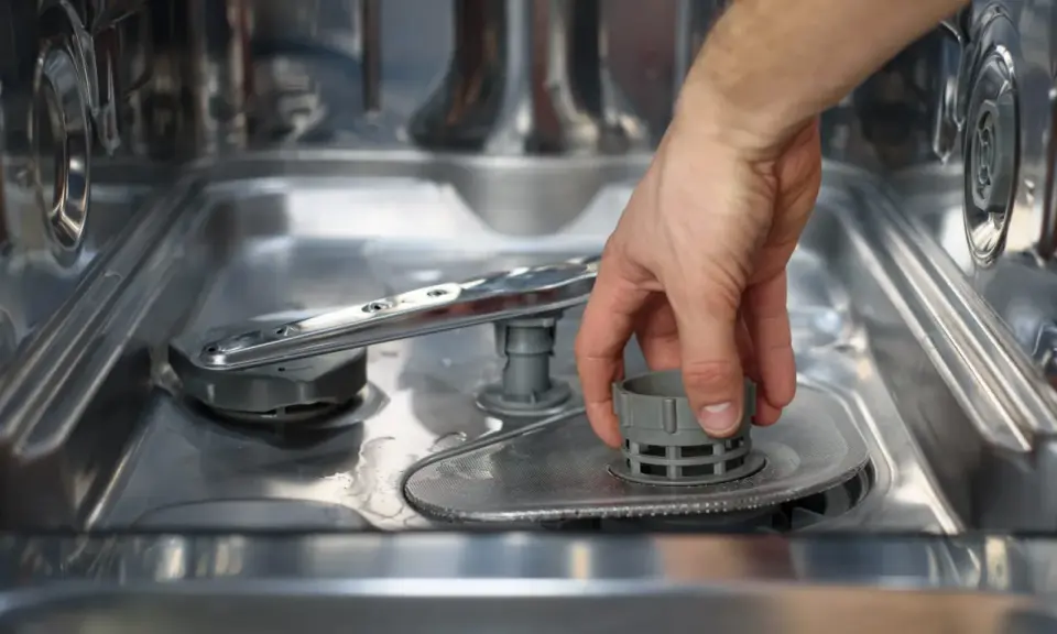Main d'homme retirant le filtre du lave-vaisselle, une étape avant le nettoyage avec de l'acide citrique.