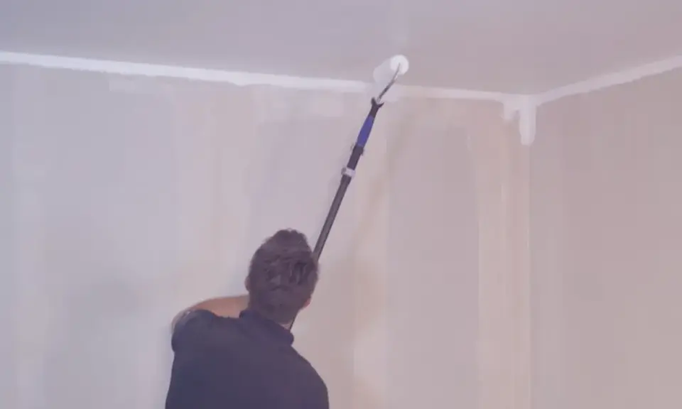 Person målar om taket med en lång roller.