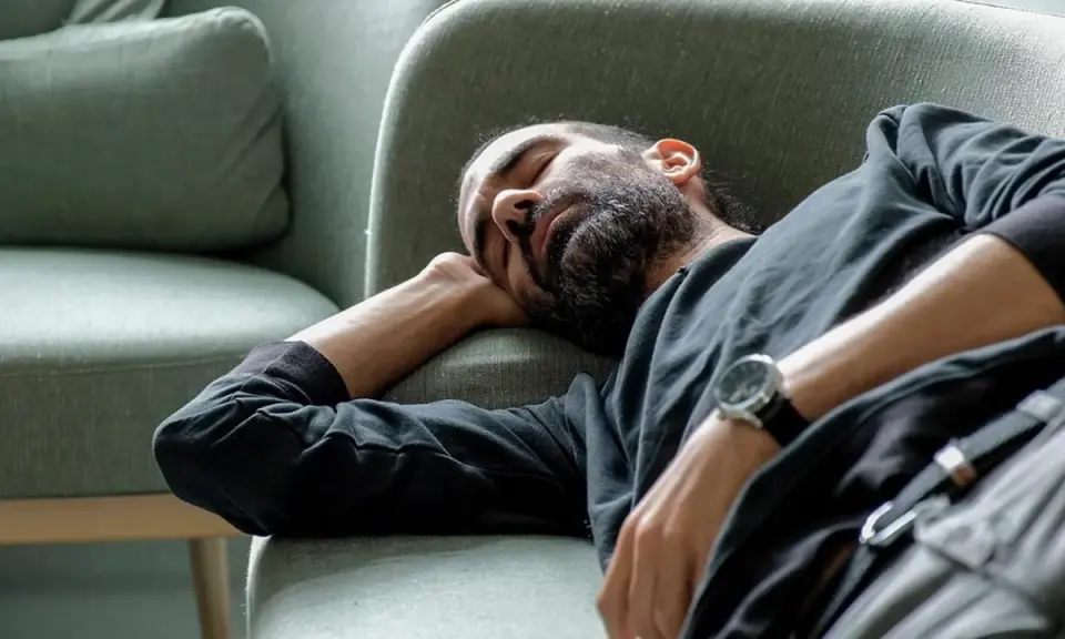 Man med skägg sover på en soffa, med armen under huvudet. Han verkar utmattad, kanske av illamående som kommer och går.