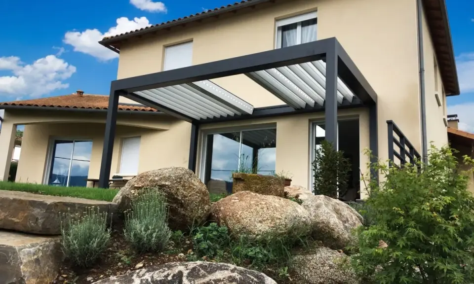 Pergola moderne sur terrasse avec vue sur une maison et un jardin rocheux.