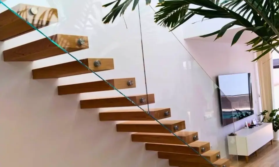 Escalera flotante de madera con **rejas de cristal** que aportan ligereza y modernidad al espacio.