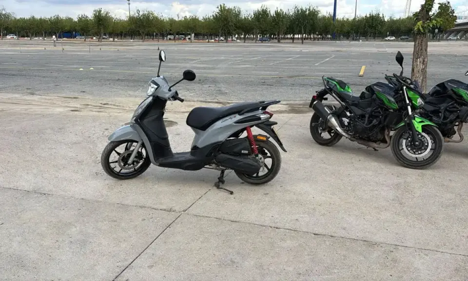 Un carnet scooter gris y dos motos verdes aparcadas en un circuito.