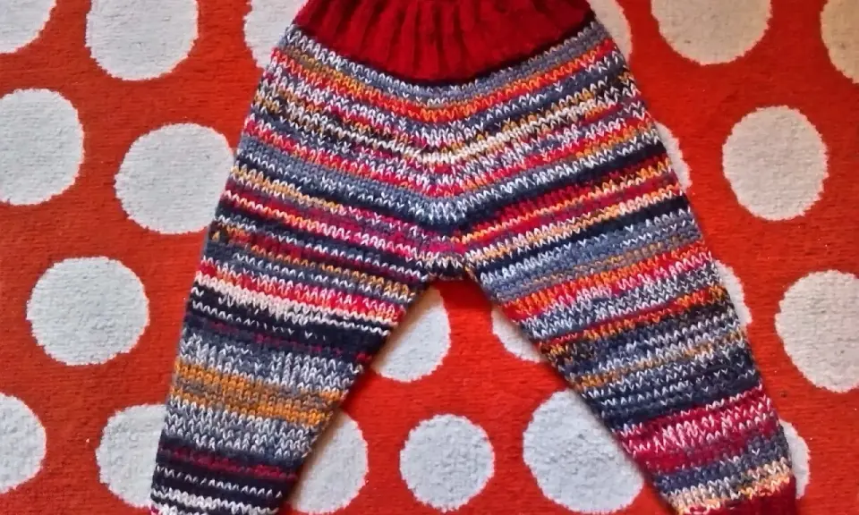 Pantalón de punto para bebé con rayas multicolores y cintura roja, sobre fondo de lunares.