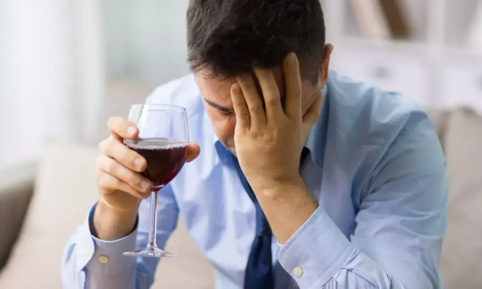 Hombre con copa de vino tinto, con la mano en la frente, buscando alivio en un vino sin histamina.