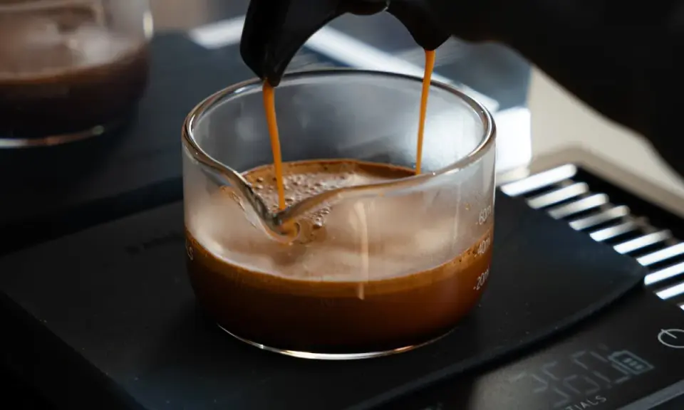 Frisch gebrühter Espresso fließt in ein Glasgefäß, die goldbraune crema de cafe bildet eine samtige Schicht.