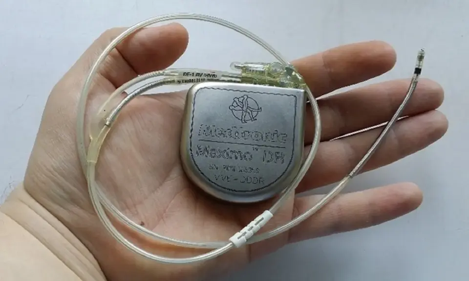 Dłoń trzyma kardiowerter Medtronic Maximo DR, urządzenie podobne do rozrusznika serca, z dwoma elektrodami.
