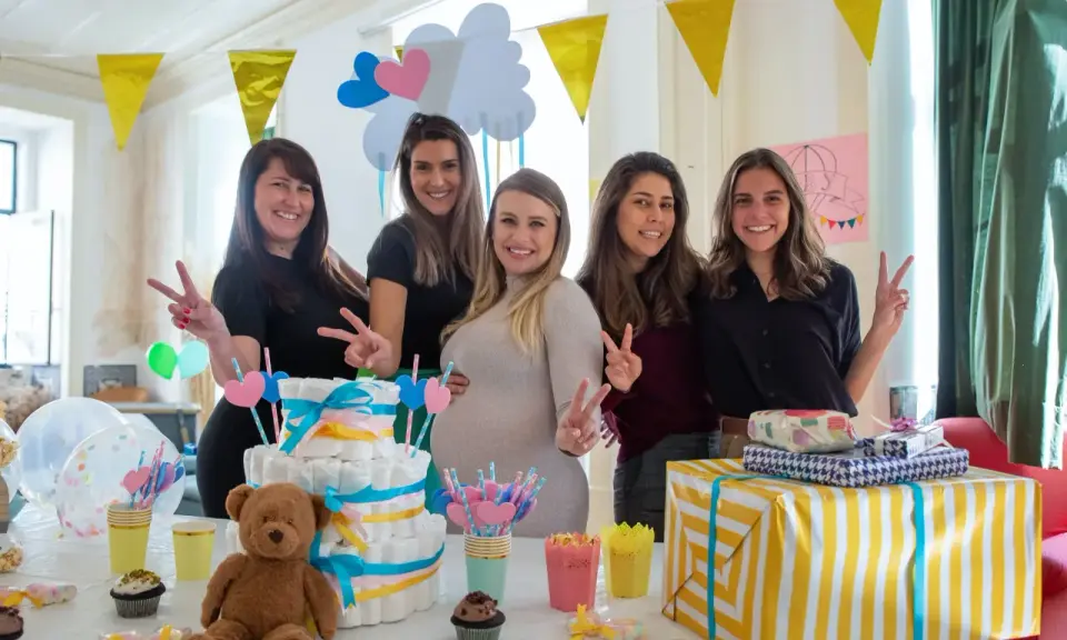 Pięć uśmiechniętych kobiet świętuje baby shower. Na stole tort z pieluch, prezenty i słodkości. To radosne wydarzenie, co to jest baby shower, pełne miłości i oczekiwania.