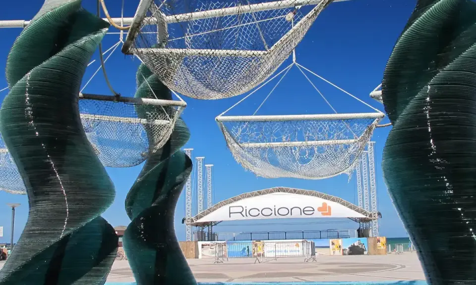 Sculture di vetro e reti sospese, con la scritta "Riccione" in lontananza. Un'idea di cosa vedere a Riccione, tra arte e mare.