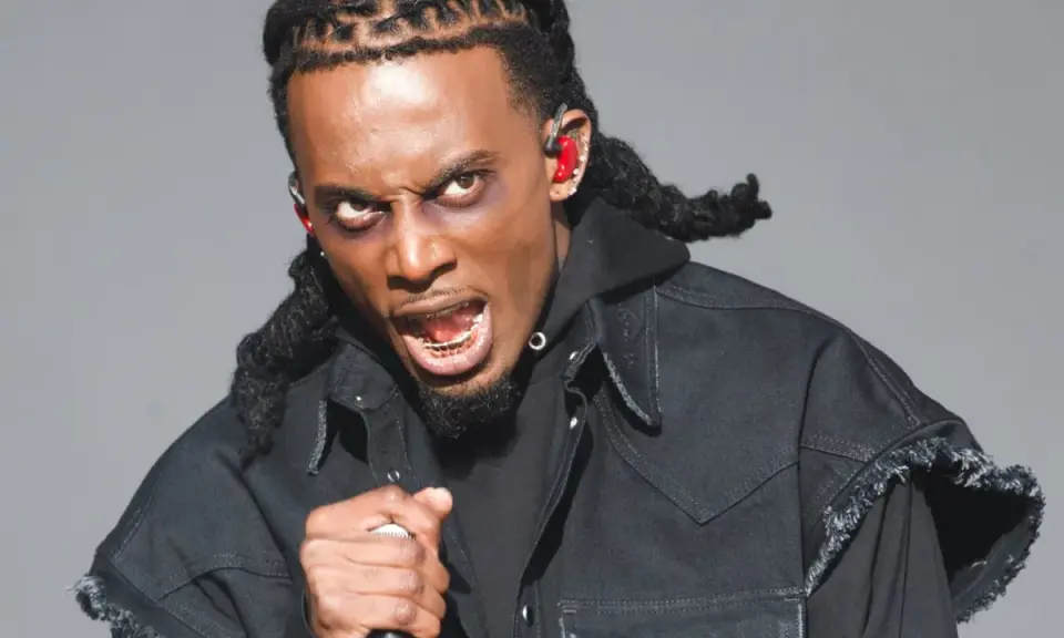 Playboi Carti z mikrofonem, w czarnej kurtce i z charakterystycznymi warkoczami. Jego ekspresja sugeruje energię znaną z jego playboi carti utworów.