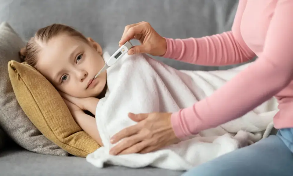 Dziecko leży pod kocem, mama mierzy mu temperaturę. Wysoka gorączka u dziecka bez innych objawów martwi.
