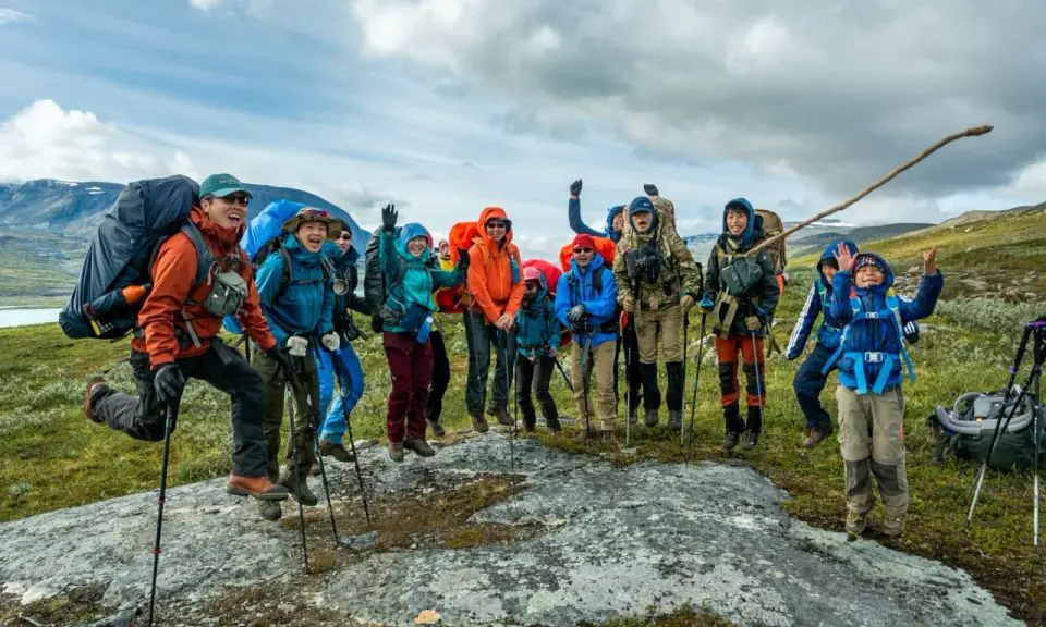 Glada vandrare, redo för Fjällräven Classic i svenska fjällen. De hoppar av glädje på en sten.