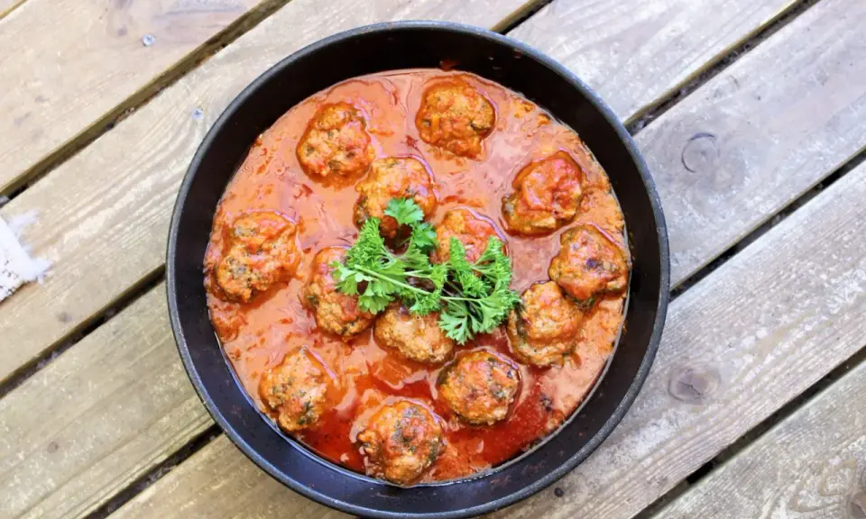 Frikadeller i tomatsås, en klassisk svensk rätt, serveras i en gjutjärnspanna. Garnerad med persilja.