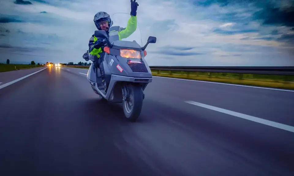 Motocyklista na skuterze 125 pozdrawia z autostrady, pokazując, że można nim jeździć po autostradzie.