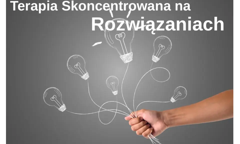 Dłoń trzymająca pęk żarówek narysowanych kredą na szarym tle.