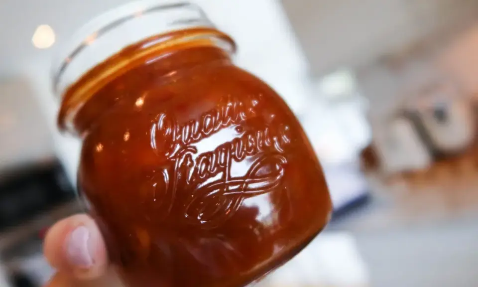 En hand håller ett glas med söt och syrlig rabarberchutney.