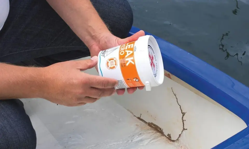 Person hält Dose mit Dichtmittel, um ein Boot abzudichten. Riss im Bootsrumpf sichtbar.