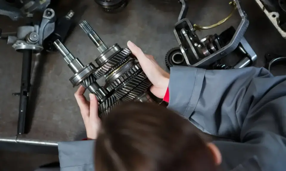 Mechanik trzyma wałki z zębatkami, przygotowując części samochodowe do wysyłki.