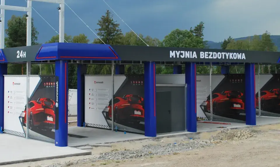 Nowoczesna myjnia bezdotykowa z niebieskimi elementami i reklamami czerwonych samochodów.