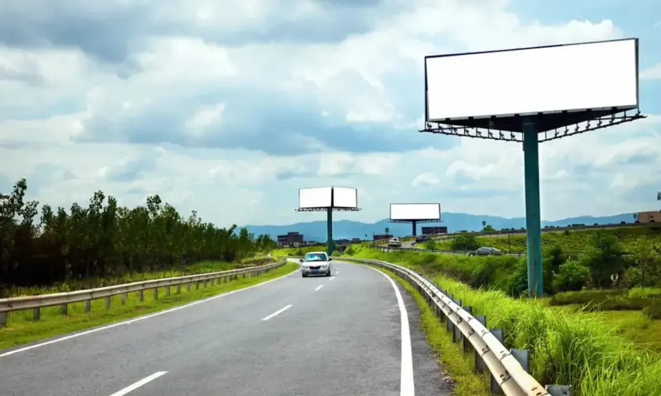 Pusta reklama przy drodze na terenie prywatnym, z widokiem na zakrzywioną autostradę i zielone wzgórza.