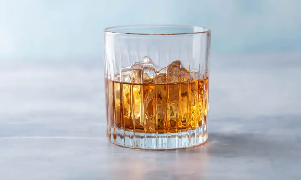 Ein Glas mit bernsteinfarbenem Getränk und Eiswürfeln, das an einen French Connection Cocktail erinnert.
