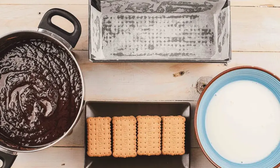 Preparando una deliciosa tarta de galletas y chocolate: chocolate derretido, galletas, molde y leche listos para mezclar.