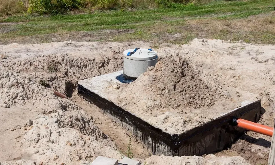 Budowa szamba: betonowa konstrukcja z rurą wylotową, przygotowana do uszczelnienia.