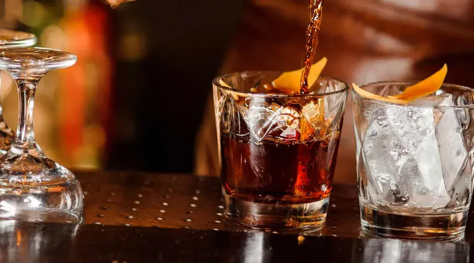 Ein Drink wird in ein Glas mit Eis und Orangenzeste gegossen. So trinkt man Whisky.